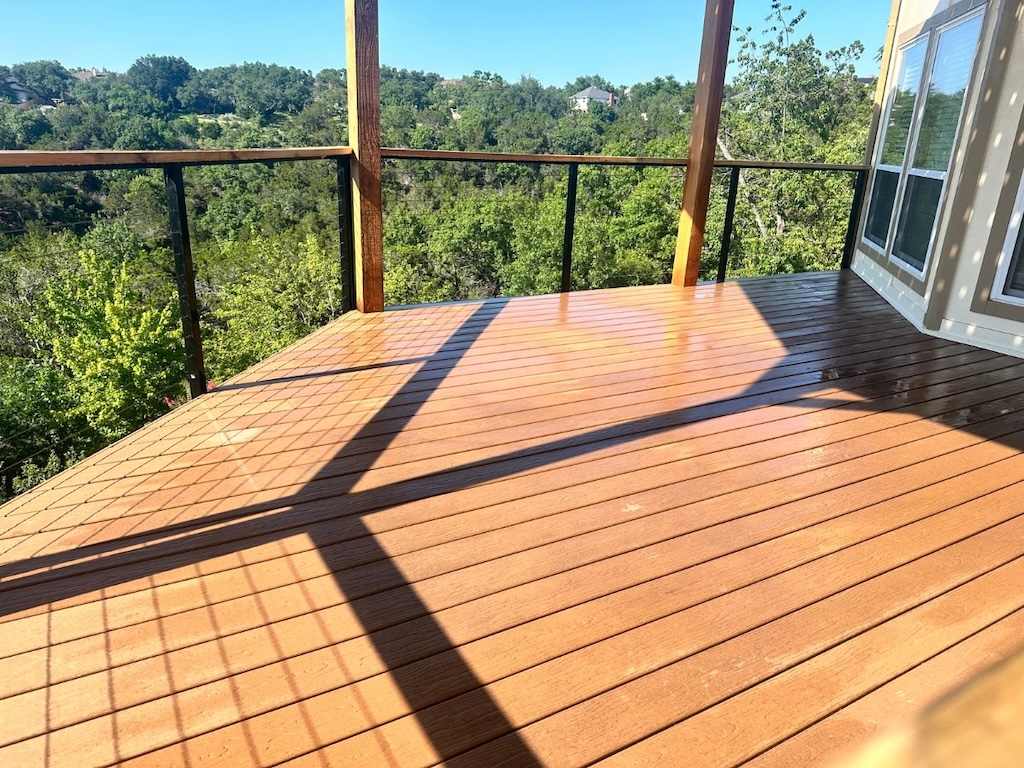 A sunny, wooden deck overlooks a lush, green forest. Shadows create geometric patterns on the deck's surface, adding a serene, peaceful ambiance.