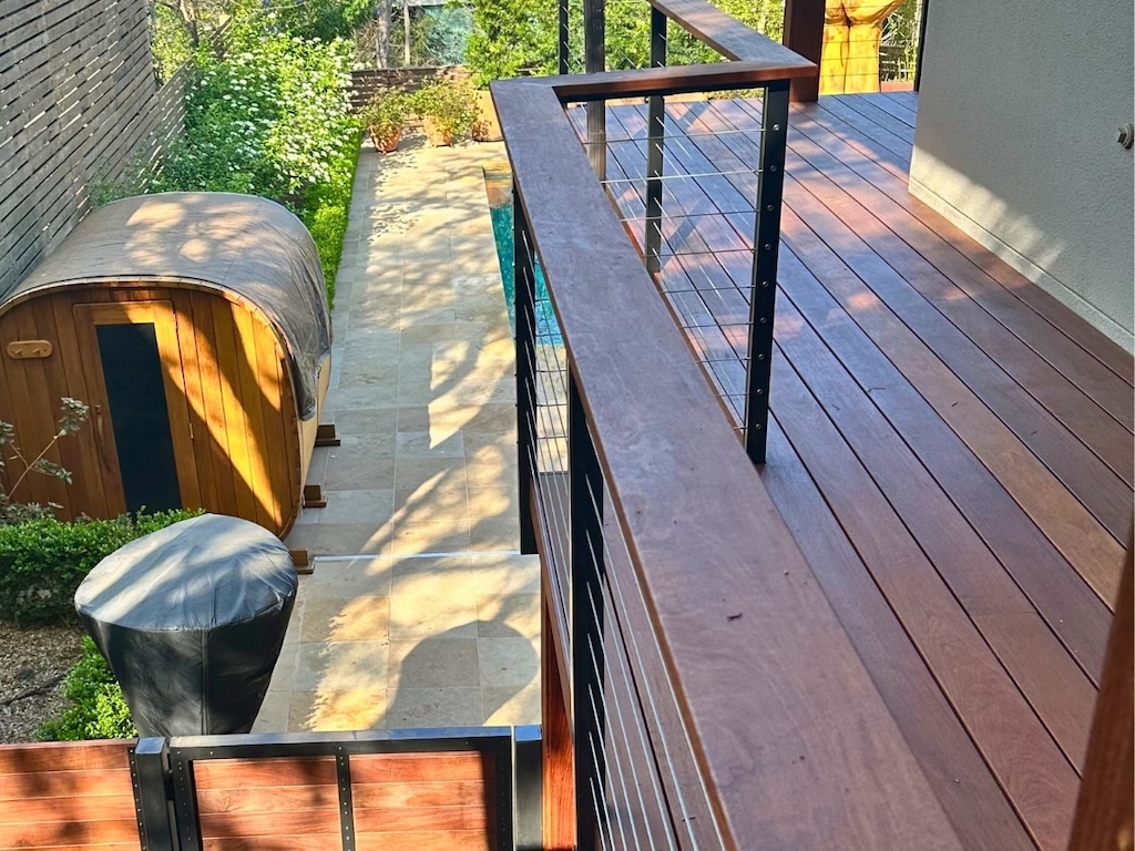 Elevated wooden deck overlooking a garden with a wooden sauna, stone pathway, and lush greenery, conveying a serene and natural atmosphere.