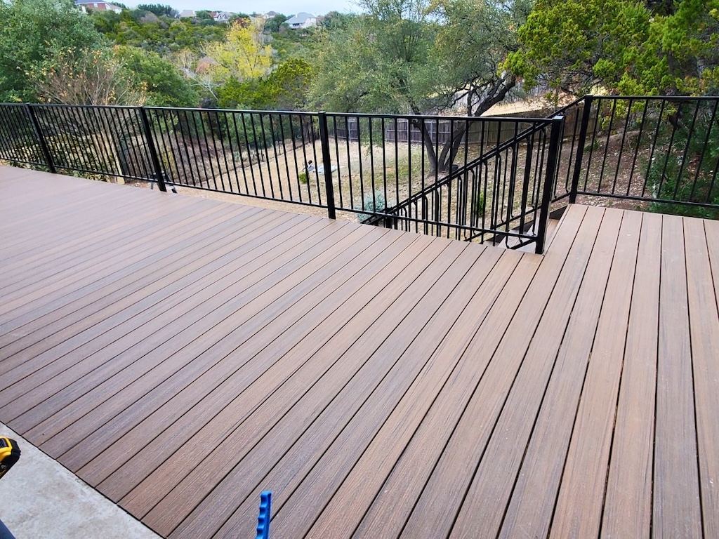 wooden deck with clean, parallel lines and a black metal railing overlooks a lush, green yard with various trees, creating a serene, natural atmosphere.