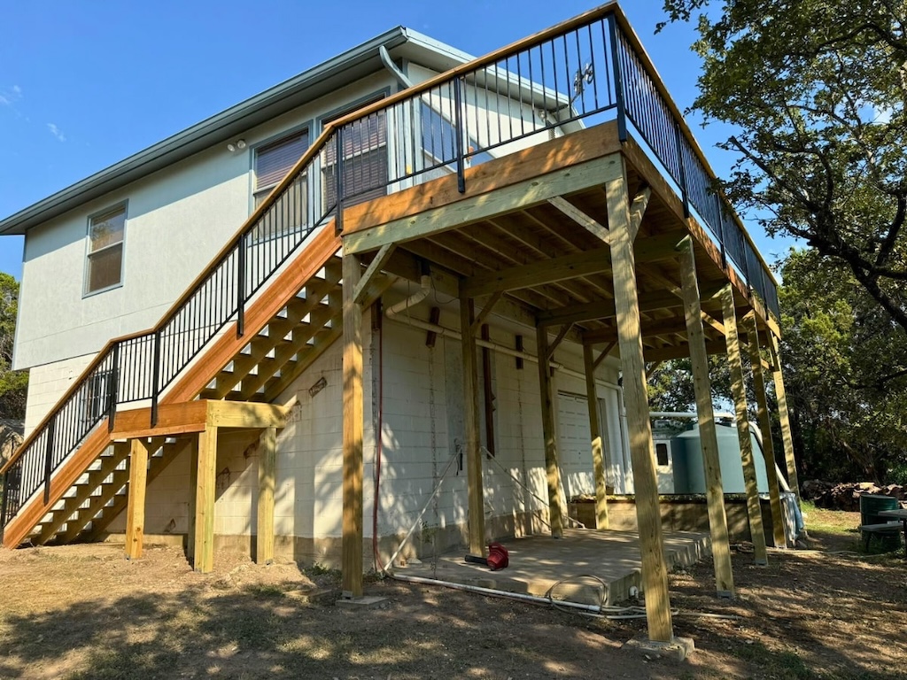 Elevated wooden deck with black railings attached to a light gray house. Sunlight casts shadows on the structure, creating a warm, serene atmosphere.