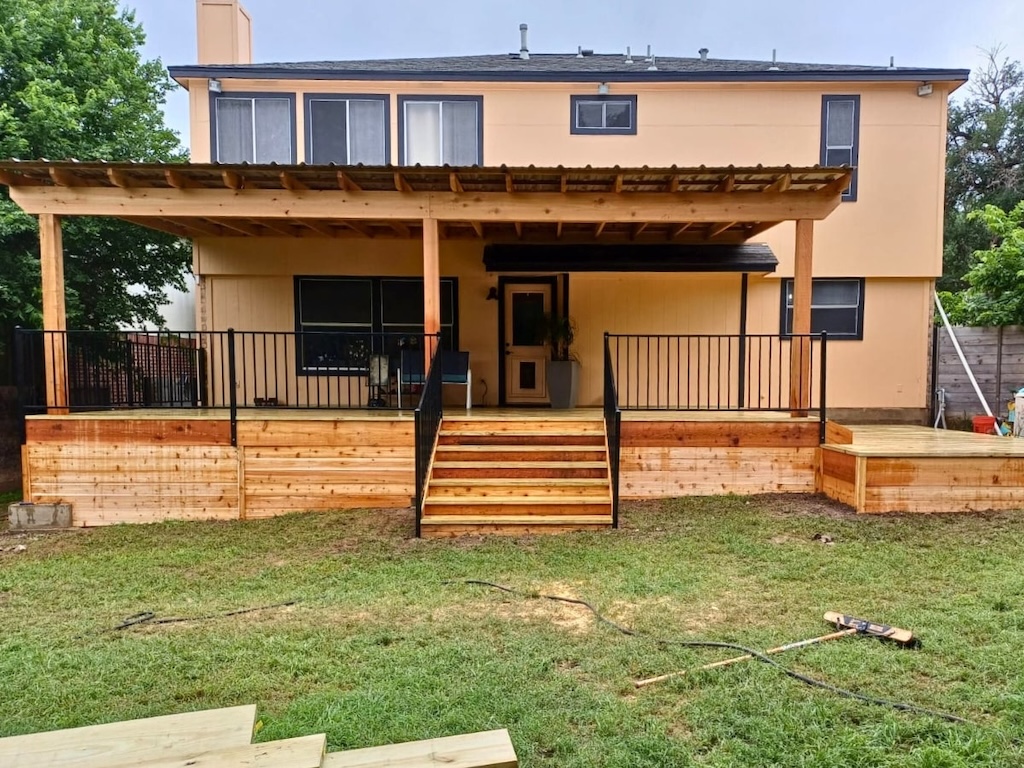 A two-story beige house features a newly built wooden deck with black railings and a pergola. The deck has steps leading down to a grassy yard.