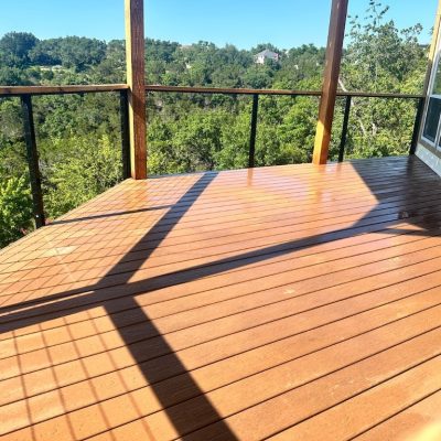 A sunny, wooden deck overlooks a lush, green forest. Shadows create geometric patterns on the deck's surface, adding a serene, peaceful ambiance.
