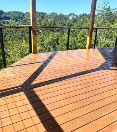A sunny, wooden deck overlooks a lush, green forest. Shadows create geometric patterns on the deck's surface, adding a serene, peaceful ambiance.