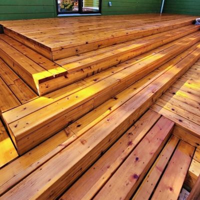 stained wooden outdoor deck with wide, tiered steps, basking in warm sunlight, creating a welcoming, natural ambiance against a green wall backdrop.