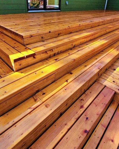 stained wooden outdoor deck with wide, tiered steps, basking in warm sunlight, creating a welcoming, natural ambiance against a green wall backdrop.