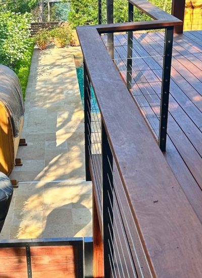 Elevated wooden deck overlooking a garden with a wooden sauna, stone pathway, and lush greenery, conveying a serene and natural atmosphere.